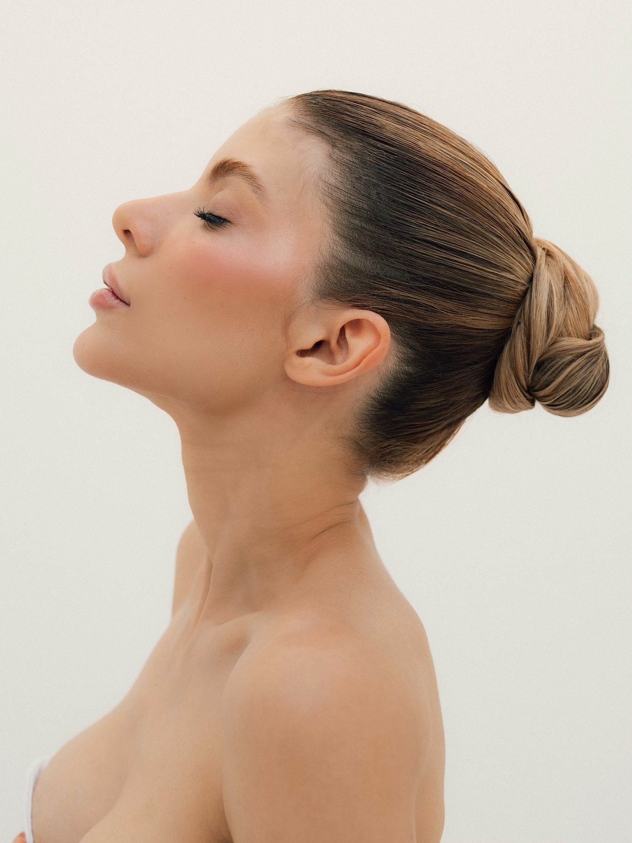 Perfil de mulher com cabelo preso em coque, pescoço alongado, sobre fundo neutro claro