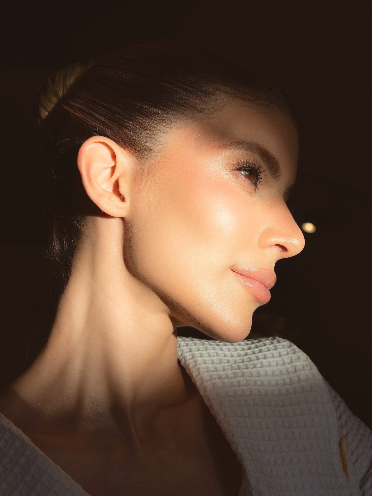 Perfil de mulher em luz lateral quente sobre fundo escuro, com pele iluminada